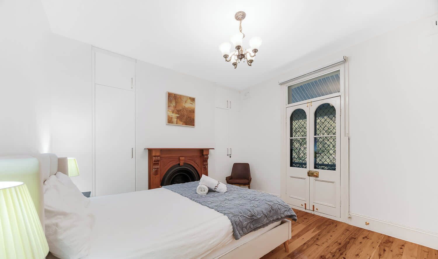 A bedroom with a bed, a fireplace, a door with glass panels, and a chandelier.