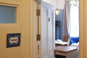 A room with a closed door, a window with a grid pattern, a table with chairs, and a hanging light fixture. - 🌊 Southsea Studio | Near the Pier | 5 Mins to the Beach! 🌊 (Portsmouth)