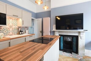 A modern kitchen with a central island, a built-in oven, a microwave, and a flat-screen TV above a fireplace. - 🌊 Southsea Studio | Near the Pier | 5 Mins to the Beach! 🌊 (Portsmouth)