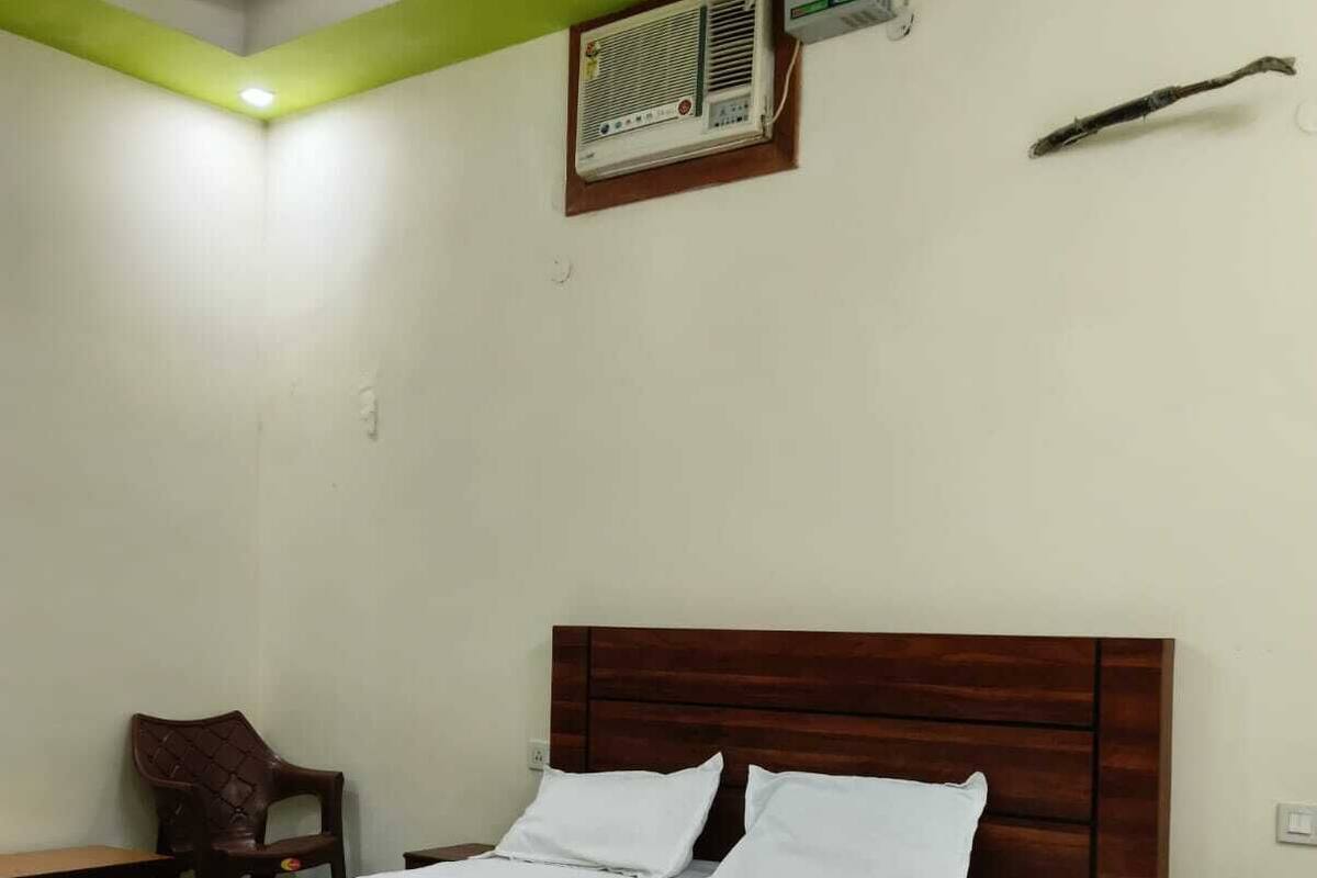 A single bed with a wooden headboard, a bedside table, a chair, and a wall-mounted air conditioning unit.