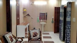 A room with a dining table, chairs, a ceiling fan, a window with a curtain, and a wall-mounted shelf. - Vishal Homestay (Ajnala)