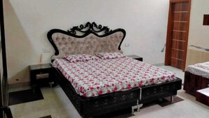 A bedroom with a bed, a nightstand, a wooden door, and a small table. - Vishal Homestay (Ajnala)