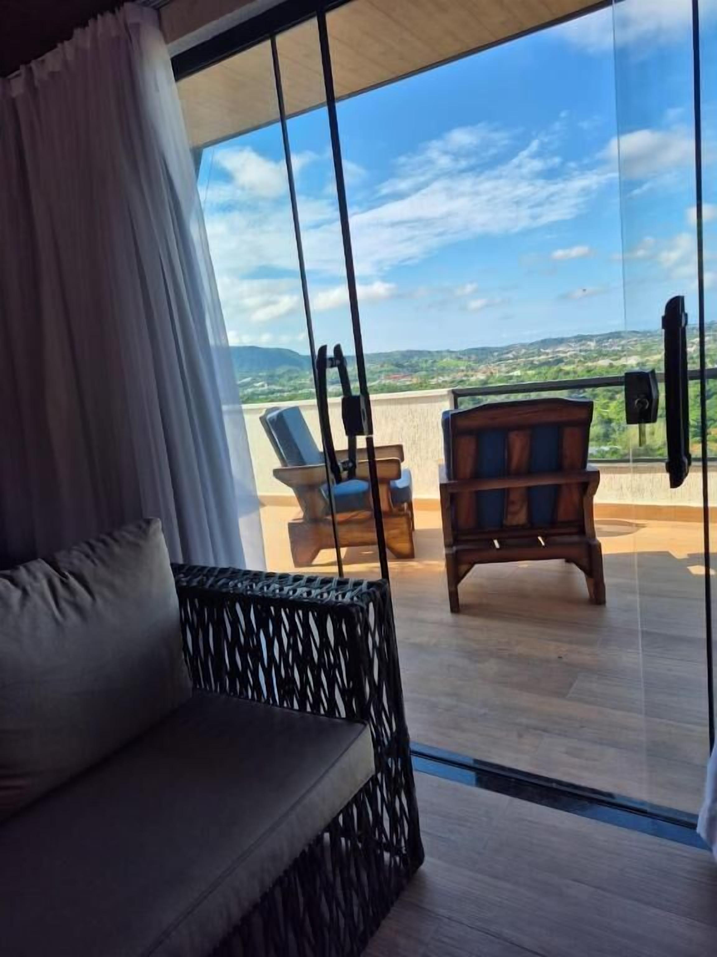 A room with a large window, a sofa, and a wooden chair.