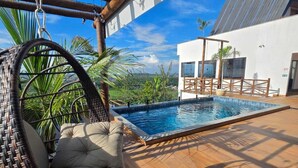 A hanging chair by a pool with a view of a white building and palm trees. - Mirante Vista Nobre (Maricá)