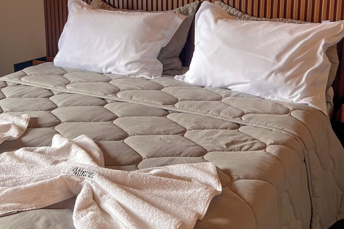 Ein Bett mit gesteppter Bettdecke, Kissen und einer Wolldecke. Darüber an der Wand hängen drei gerahmte Bilder.