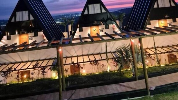 A row of modern, triangular-roofed buildings with solar panels, connected by a covered walkway, set against a twilight sky. - Mirante Vista Nobre (Maricá)