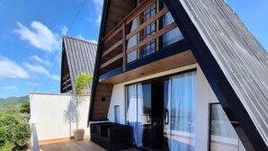 A modern house with a sloped roof, large windows, and a wooden deck. - Mirante Vista Nobre (Maricá)