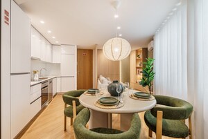 Una cocina moderna con armarios blancos, una mesa de comedor con sillas tapizadas en verde y una lámpara colgante.