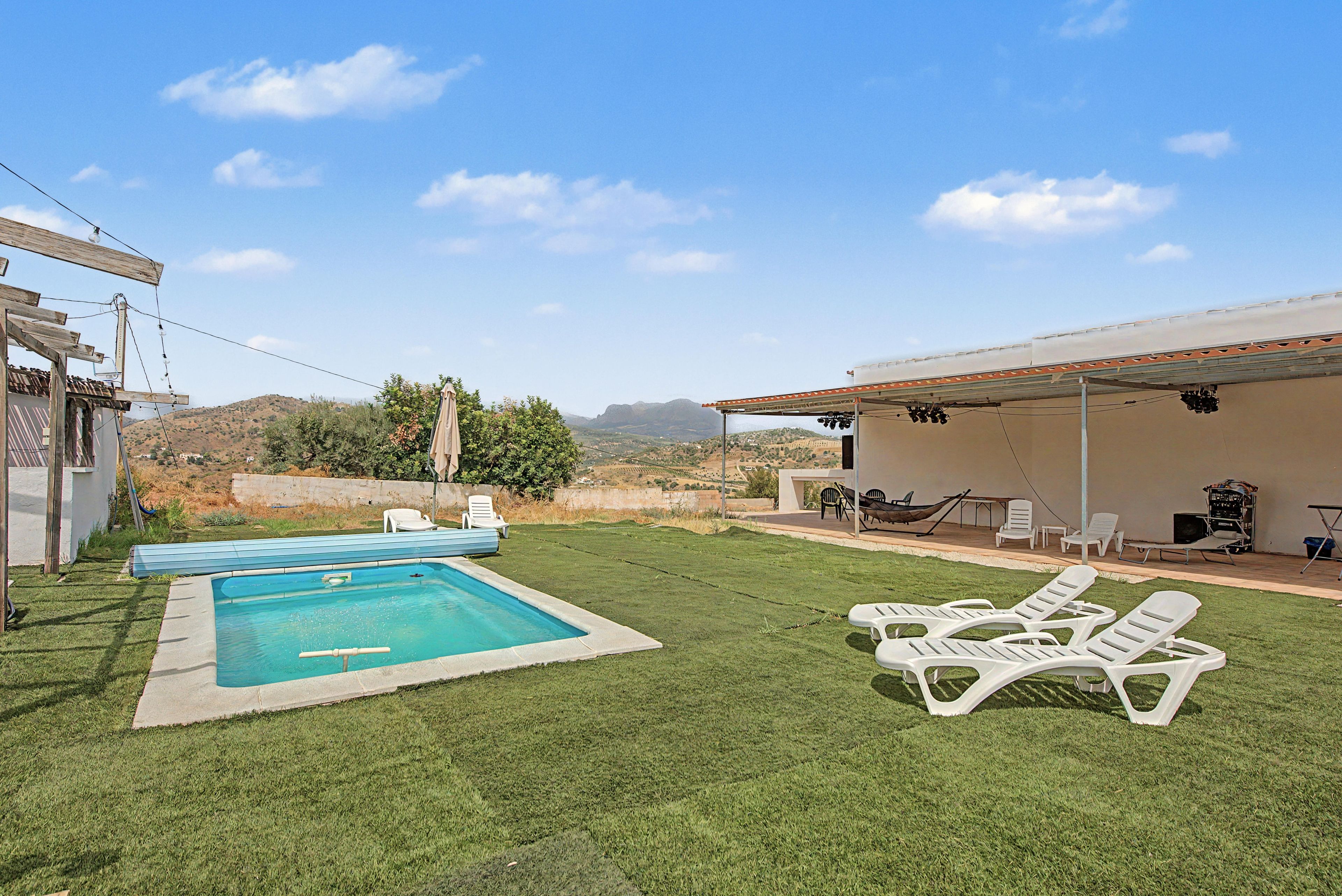 Patio trasero con piscina, sillas de descanso blancas y zona cubierta.
