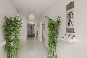 En hall med modern design, med ett vitt golv, en hängande lampa och en vägghylla med små växter.
