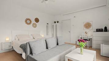 Et moderne, minimalistisk soveværelse med en grå sofa, et lille hvidt bord og en loftsvift.
