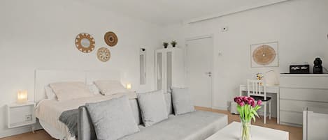 Un dormitorio moderno y minimalista con un sofá gris, una mesita blanca y un ventilador de techo.