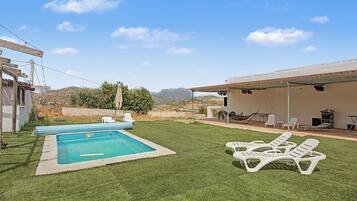 Ein Garten mit Swimmingpool, weißen Liegestühlen und einer überdachten Terrasse.