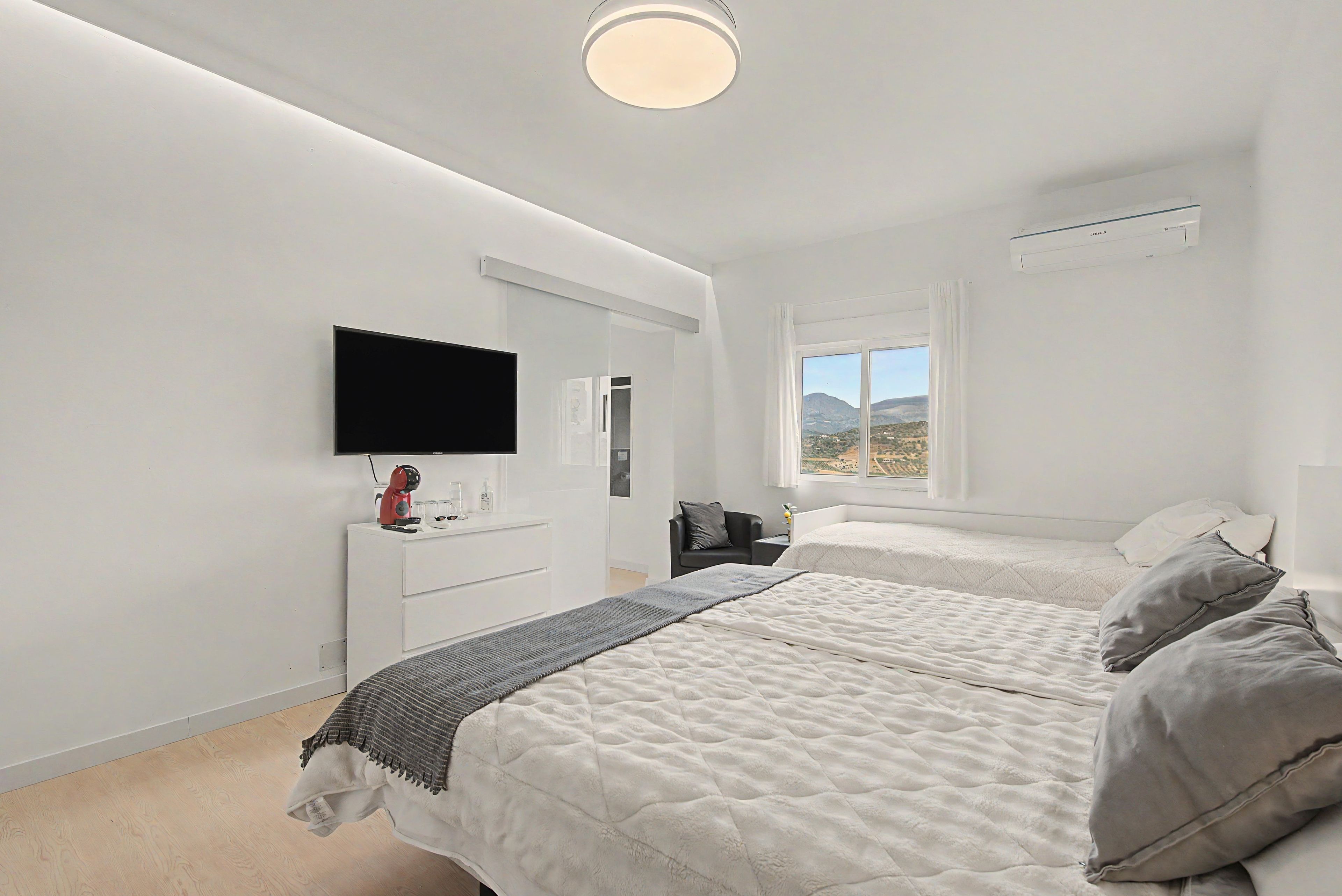 Een slaapkamer met twee bedden, een televisie, een raam met uitzicht en een witte dressoir.