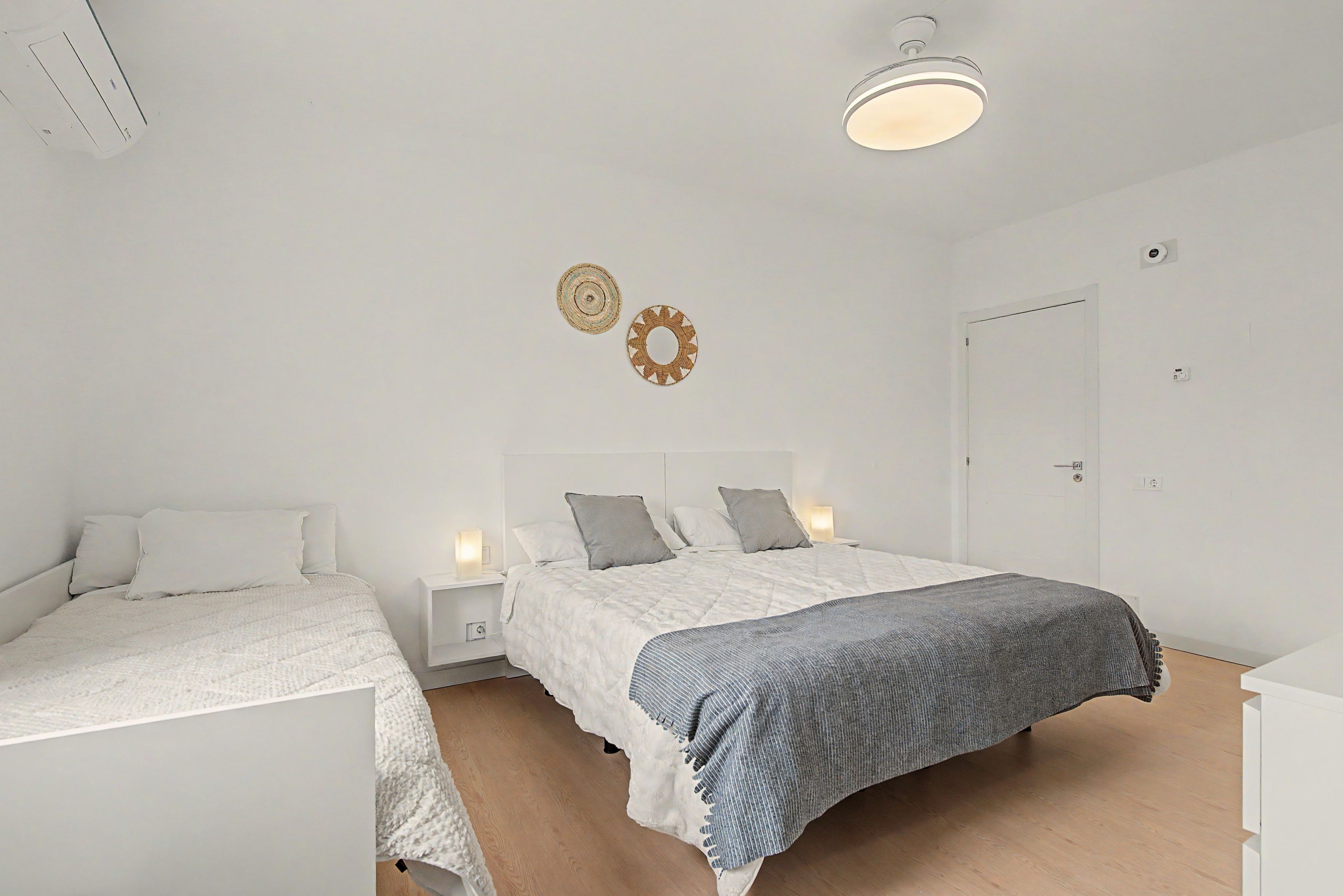 A bedroom with two beds, a bedside table with a lamp, a door, and a ceiling light fixture.