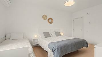 A bedroom with two beds, a bedside table with a lamp, a door, and a ceiling light fixture.