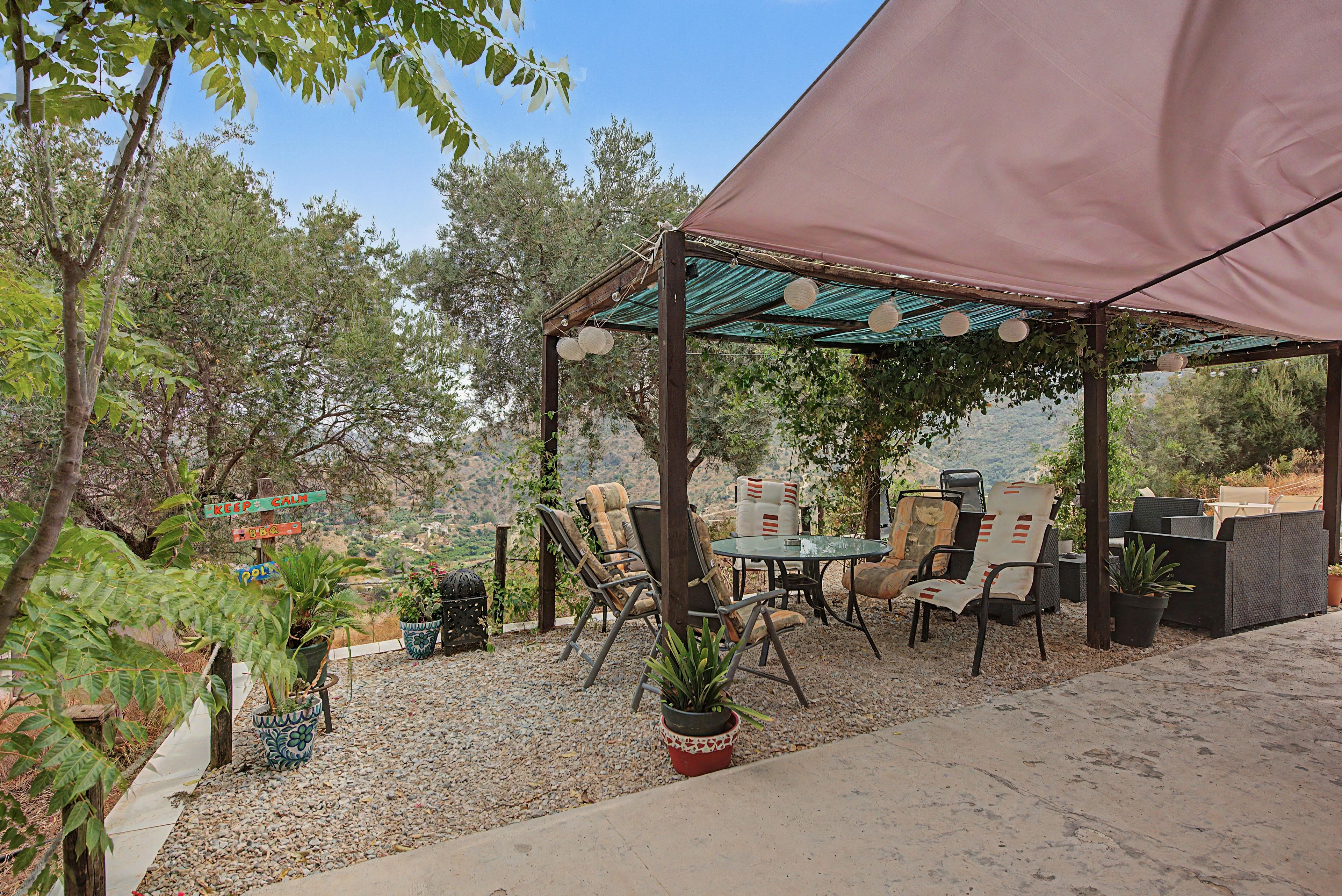Un patio al aire libre con una mesa y sillas, rodeado de plantas en macetas y vistas al paisaje.