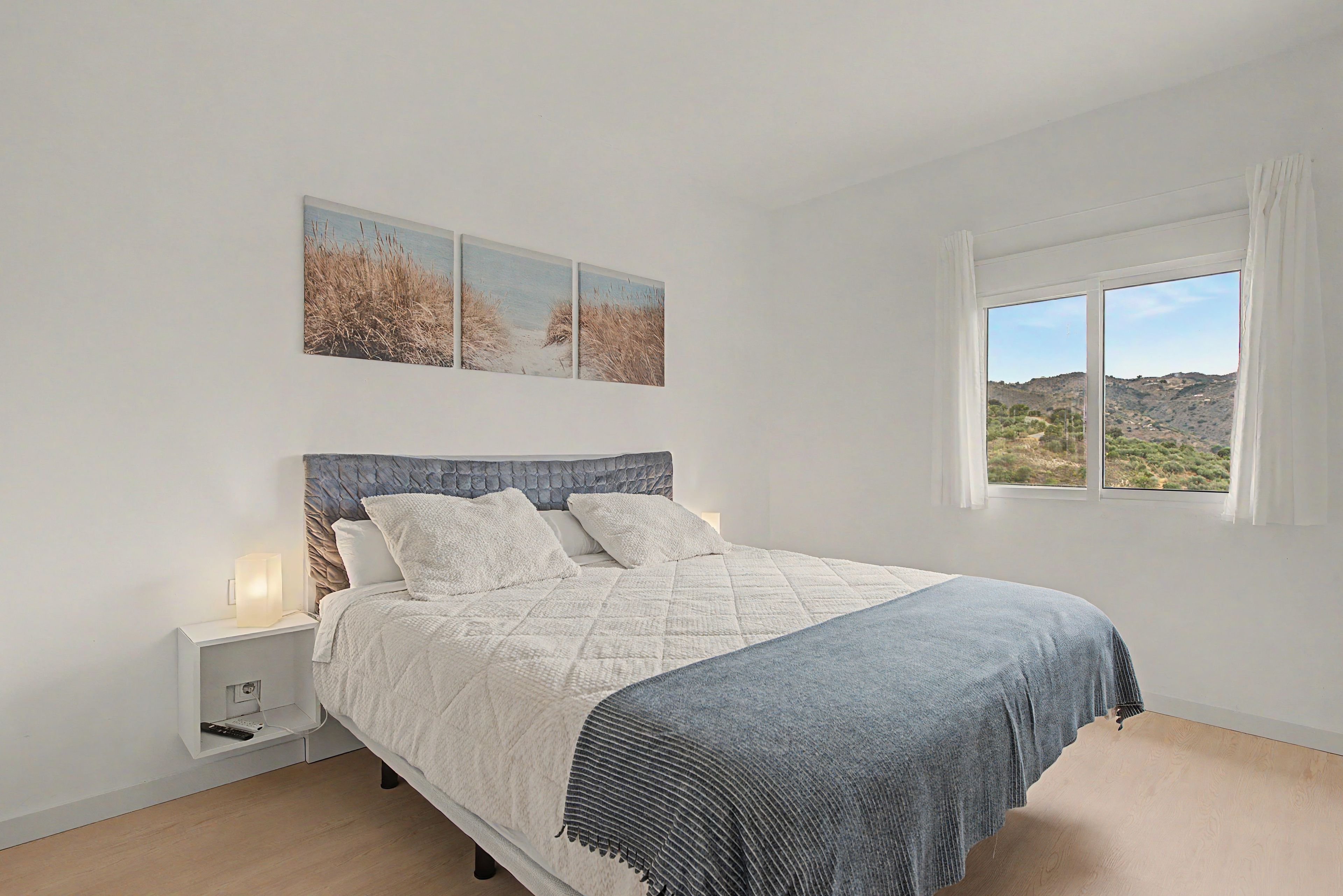 Un dormitorio con una cama, una mesita de noche, una ventana con vistas y decoración en la pared.