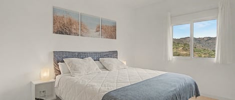 Ein Schlafzimmer mit Bett, Nachttisch, Fenster mit Blick und Wandkunst.