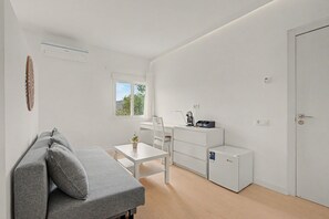A modern, minimalist room with a grey sofa, a small white table, a coffee machine, and a compact refrigerator. - Jingtu Wellness & Spa Vairochana (Romo Cuevas)