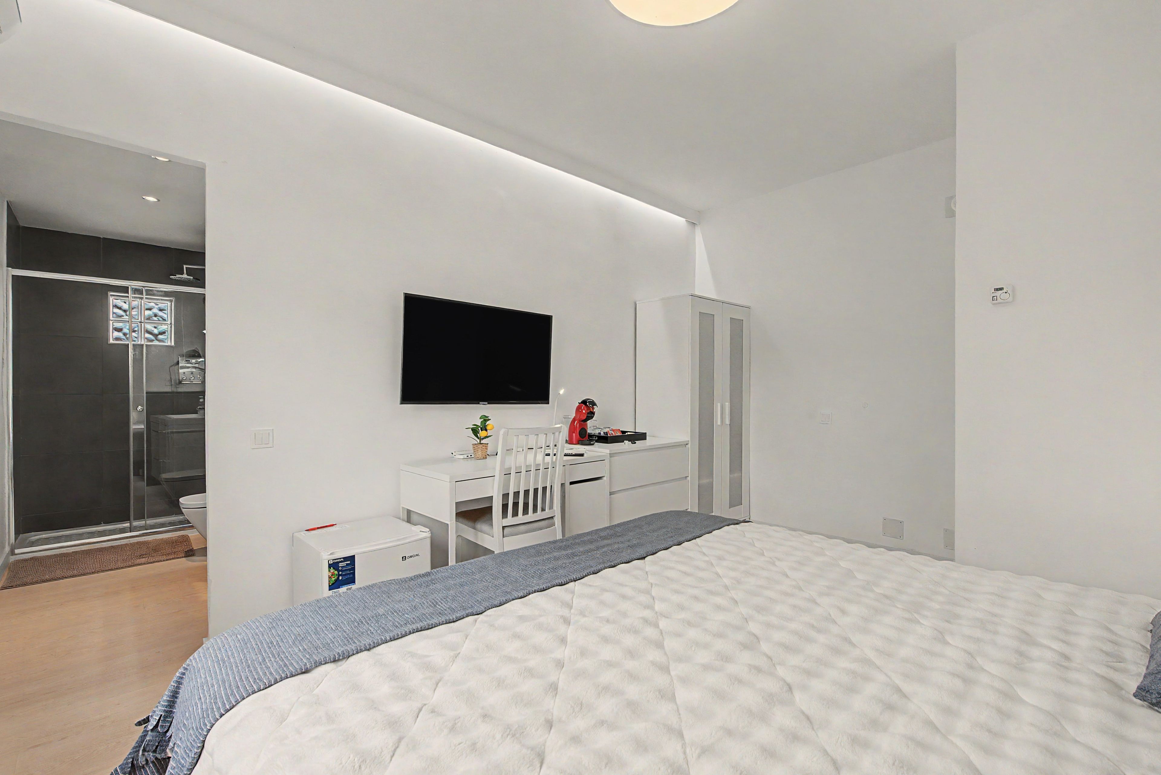 Ein modernes Schlafzimmer mit einem Bett, einem Schreibtisch, einem Stuhl, einem Fernseher und einem Kleiderschrank.