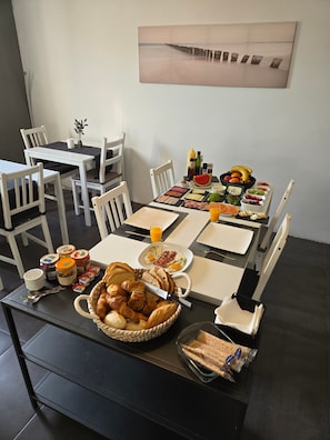 Een ontbijt opstelling met een tafel, stoelen en diverse etenswaren, zoals brood, fruit en toevoegingen.