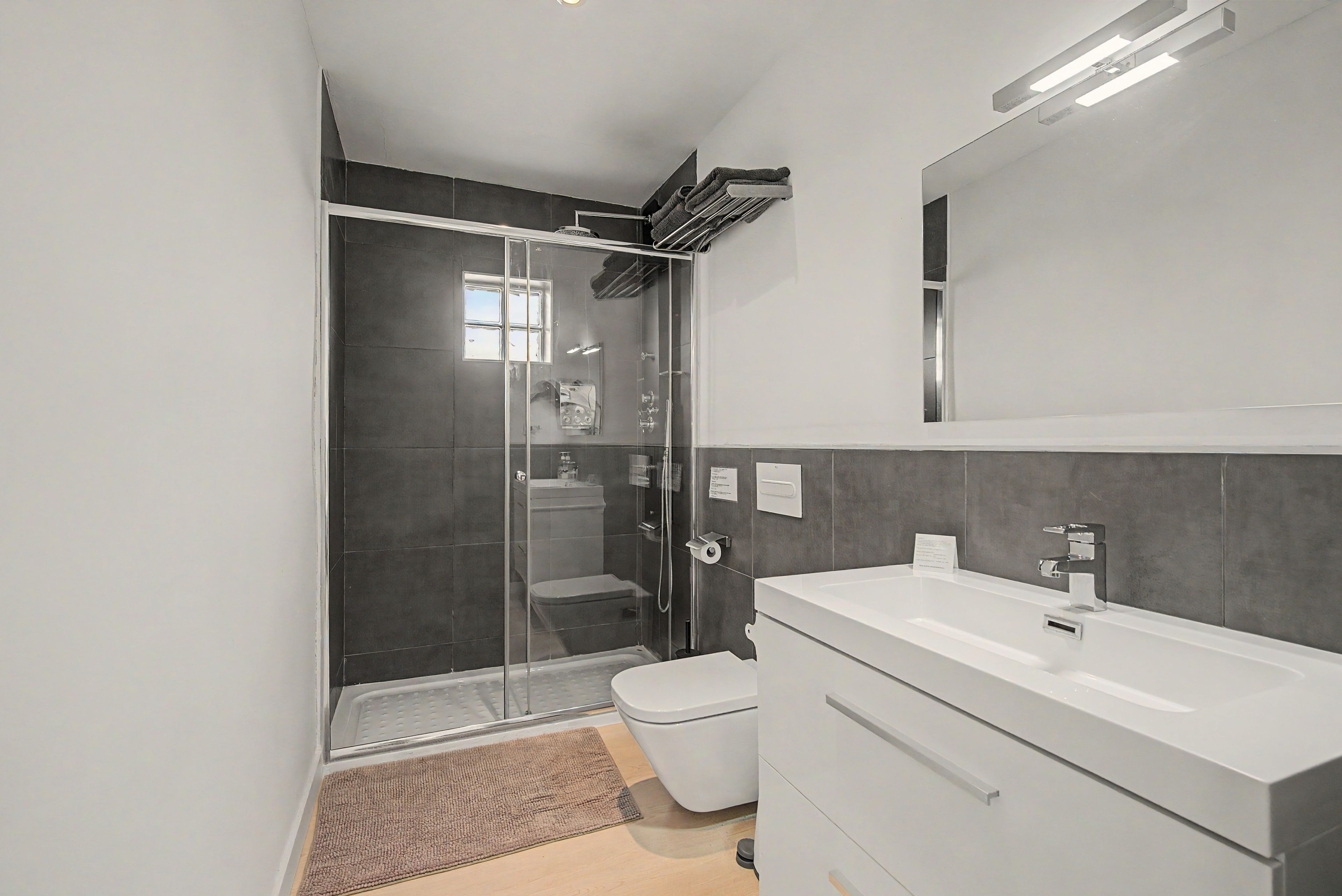 A modern bathroom with a glass-enclosed shower, a white sink, and a large mirror.