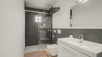 A modern bathroom with a glass-enclosed shower, a white sink, and a large mirror.