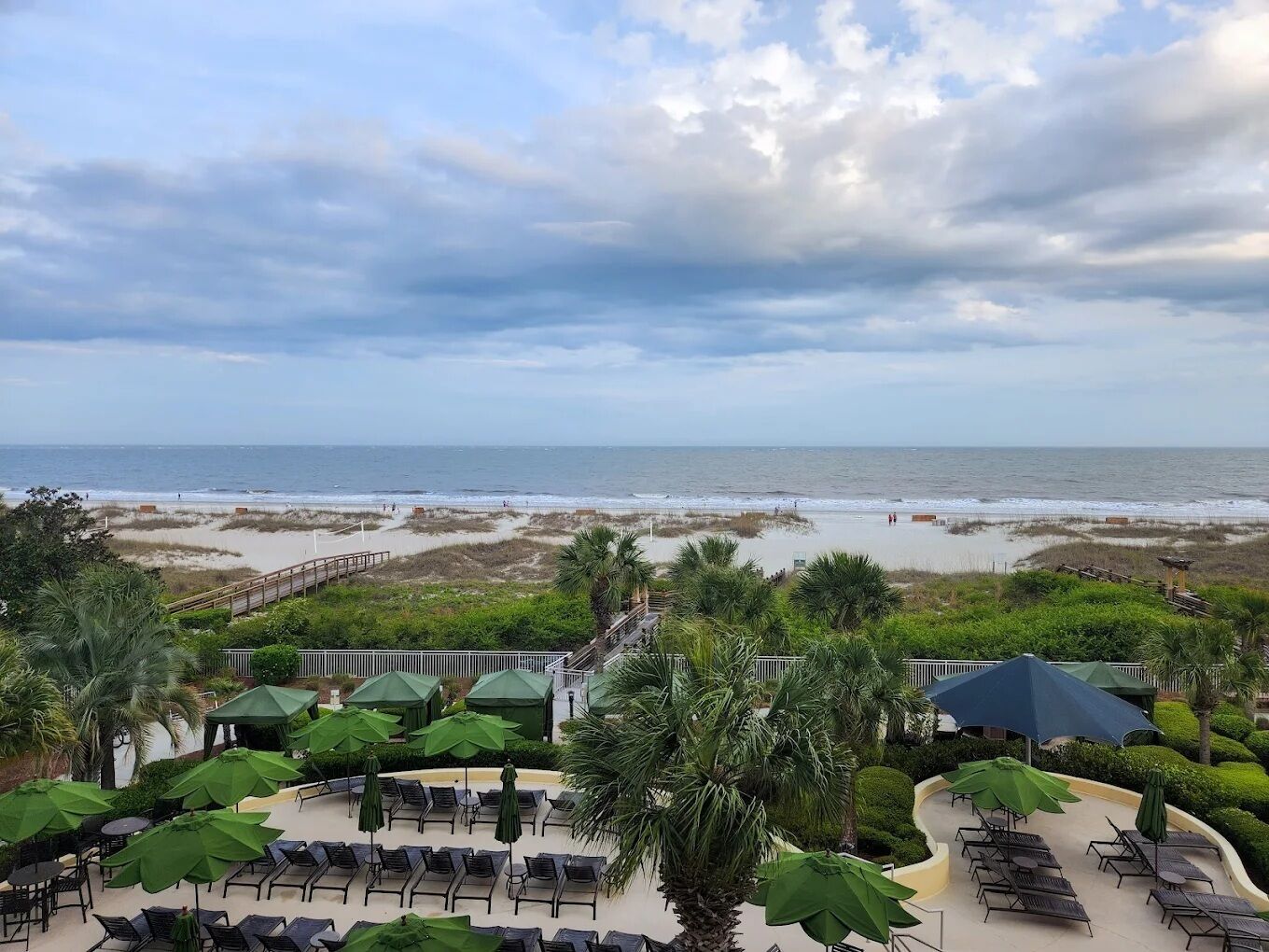 Vista a la playa con un área de patio que incluye sillones de sol y sombrillas.