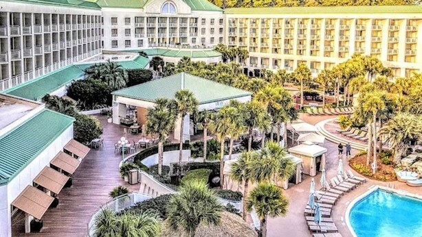 Ein Hotel mit mehreren Gebäuden, einem Schwimmbad und einem angelegten Innenhof mit Palmen.