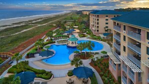 Ein Resort mit einem zentralen Schwimmbad, Blick auf den Strand und mehreren Gebäuden mit Balkonen.