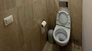 A modern bathroom with a toilet, a trash bin, and a toilet paper holder on the wall. - Lama Rooms (Warsaw)