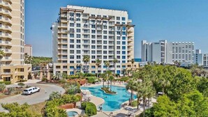 Un hotel con varias construcciones altas, una piscina central y zonas verdes circundantes.