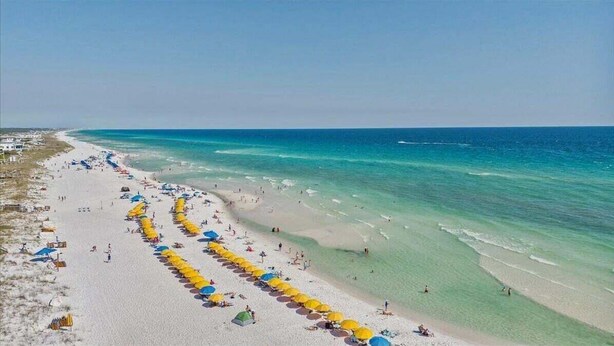 Una playa con sombrillas, gente, agua cristalina y cielo despejado.