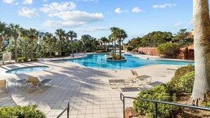 Piscina con sillas de descanso, palmeras y terraza de baldosas.