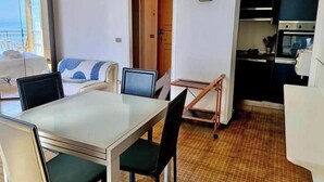 A compact hotel room with a dining table, chairs, a bed with a view, a kitchenette, and a small bathroom. - Hostdomus - Bay Apartment (Laigueglia)