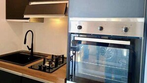 A modern kitchen with a built-in oven, a gas stove, and a stainless steel sink. - Hostdomus - Bay Apartment (Laigueglia)