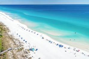 Ein Strand mit weißem Sand, klarem türkisblauem Wasser und einer langen Reihe von Strandsonnenschirmen.