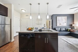 Eine moderne Küche mit Geschirrspüler, Kühlschrank, Pendelleuchten und einem Essbereich mit Sofa und Teppich.