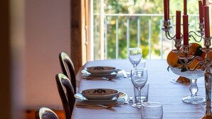 Une table à manger dressée avec des assiettes, des verres et un chandelier, donnant sur un paysage verdoyant par la fenêtre.