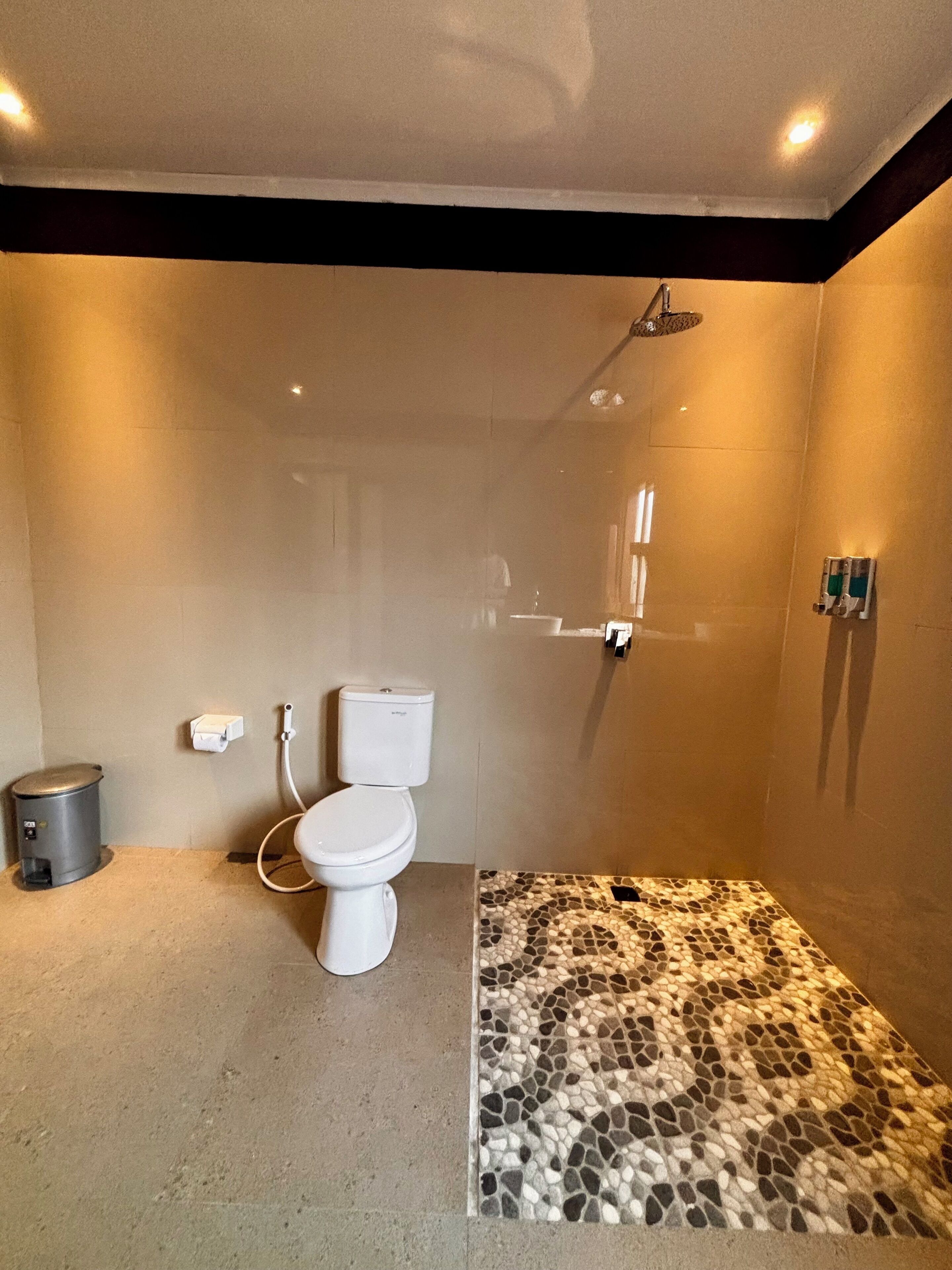 A bathroom with a toilet, a shower, a trash bin, and a mosaic floor.