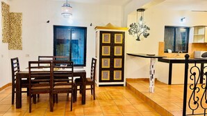 A dining area with a table and chairs, a kitchen area with a counter and sink, and a decorative wall piece. - Independent Bungalow for rent at Siolim. Next to main market with parking for 2 (Siolim)