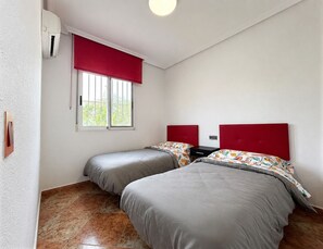 A room with two beds, a window with red blinds, a thermostat, and a wall-mounted light fixture. - Holiday Home Torrevieja (Torrevieja)