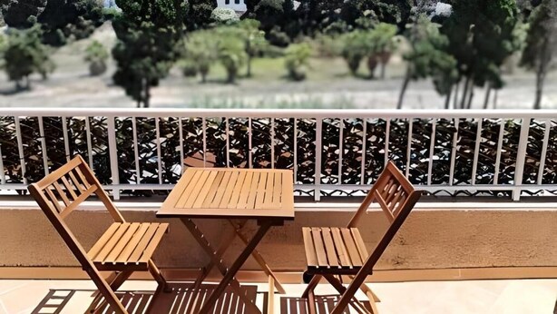 Un balcone con tavolo e sedie, una ringhiera bianca e vista su alberi e un edificio.