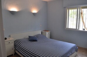 A bedroom with a bed, nightstands, and a window with bars. - Apartment with sea views in Cumbre del Sol (Cumbre del Sol)