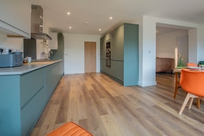 A modern kitchen with a central island, wooden flooring, and a dining area with a bright orange chair. - Stylish Home Near Scotch Corner For Work Leisure (Richmond)
