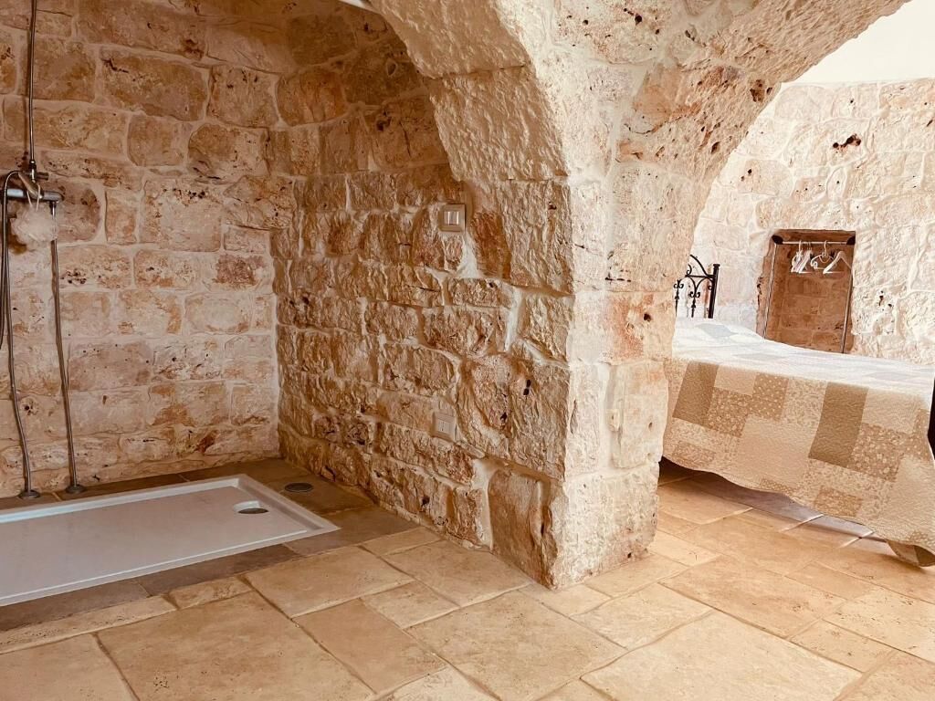 A stone-walled room with a checkered bedspread, a small table, and a wall-mounted heater.