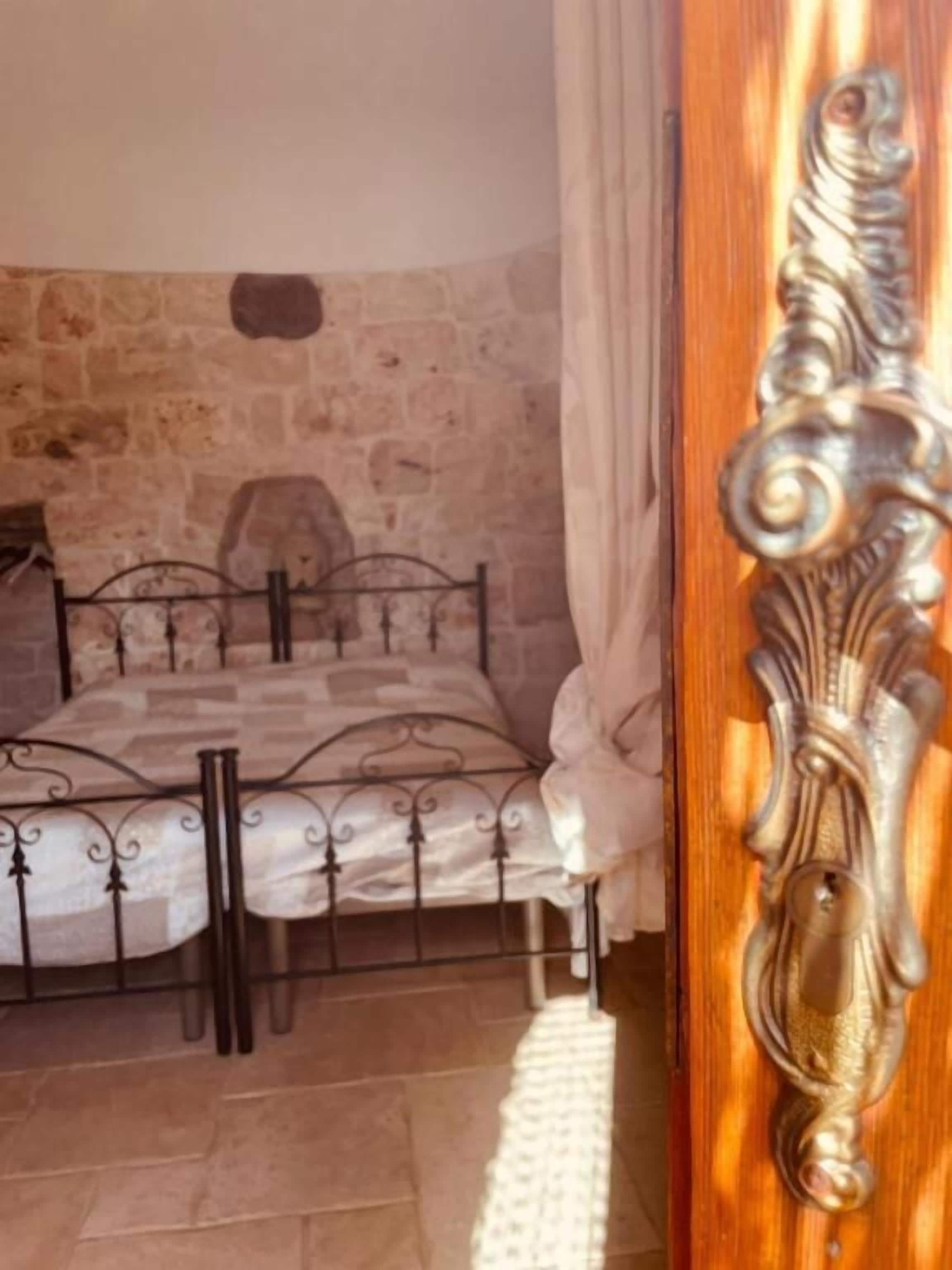 A bedroom with a stone wall, a metal bed frame, and a wooden door with an ornate handle.