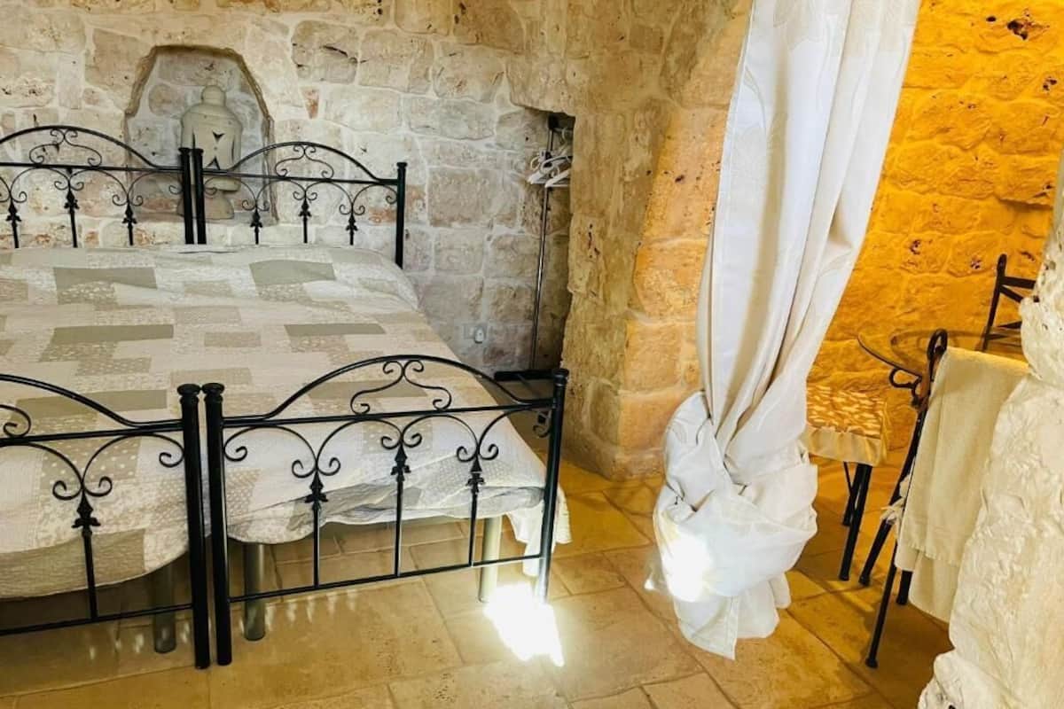 Una habitación con paredes de piedra, una cama, una silla y una mesa.