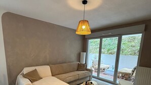 Ein modernes Wohnzimmer mit einer Couch, einem runden Hocker, einer Pendelleuchte und Blick durch eine Glastür.